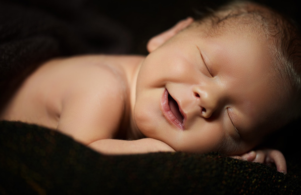Gelukkig pasgeboren baby lacht in zijn slaap op een donker - Foto, afbeelding