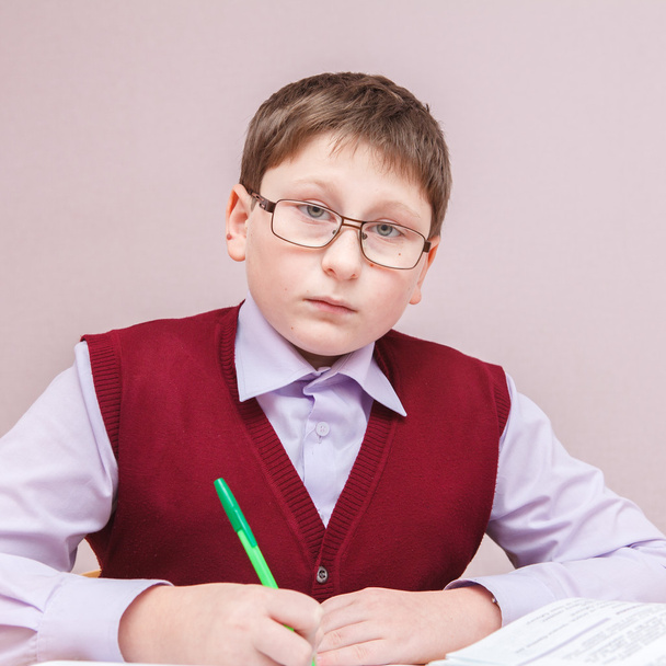 boy with glasses sitting at a desk writing - Foto, imagen