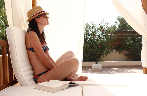 Young beautiful woman reads a book and relaxes over a pool bed close to the sea, Formentera, Spain - Фото, зображення