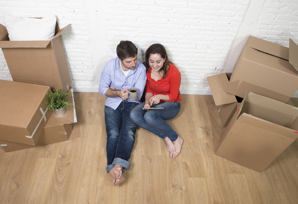 young couple sitting on floor moving in new house using digital  - Photo, Image
