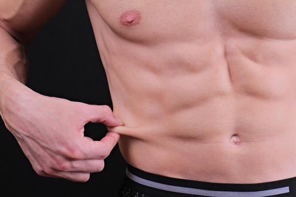Body fat percentage. Muscular man measures level of fat on his body close up. - 写真・画像