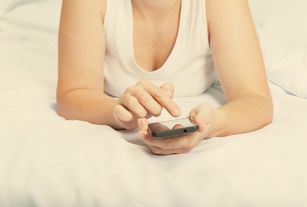 Νεαρή καυκάσιος γυναίκα στο κρεβάτι με smartphone  - Φωτογραφία, εικόνα
