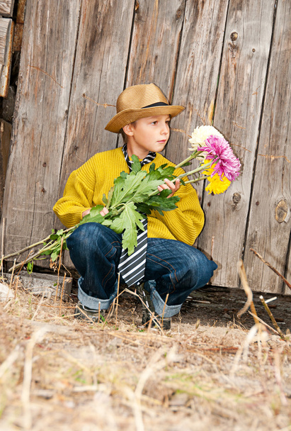 A boy with a bouquet of chrysanthemums against a wooden fence. - Fotografie, Obrázek