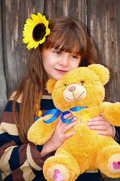 Girl with teddy bear against a wooden fence. - Фото, зображення