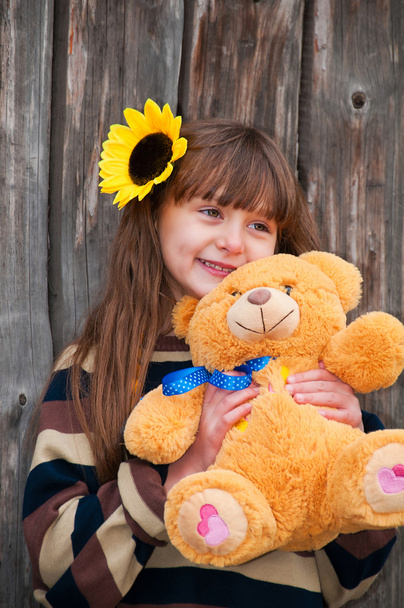 Girl with teddy bear against a wooden fence. - Fotoğraf, Görsel