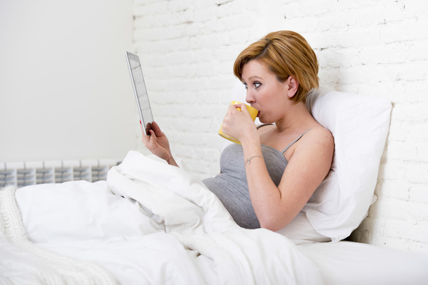 attractive woman on bed using digital tablet pad reading morning online news in internet having coffee - Zdjęcie, obraz