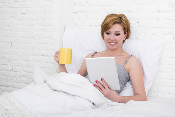 привлекательная женщина на кровати с помощью цифрового планшета чтение утренние онлайн новости в Интернете с кофе
 - Фото, изображение