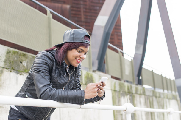 Mujer sonriente buscando mensaje en el teléfono inteligente en la calle, concepto de estilo de vida urbano
. - Foto, imagen