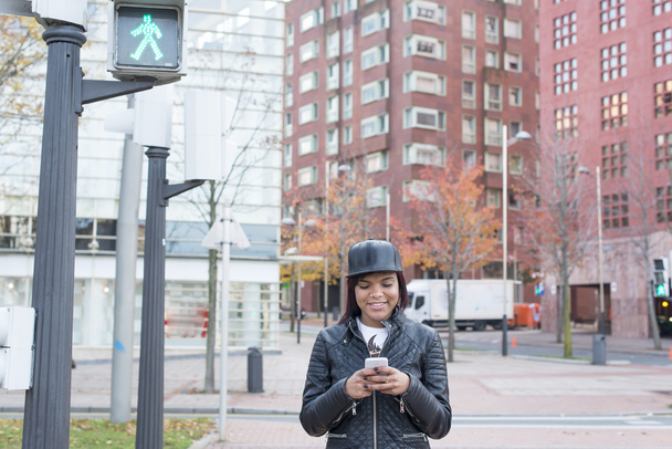 Mujer sonriente buscando mensaje en el teléfono inteligente en la calle, concepto de estilo de vida urbano
. - Foto, Imagen