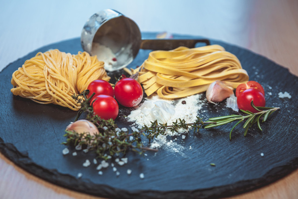 Красивые свежие спагетти на доске со специями и помидорами
 - Фото, изображение