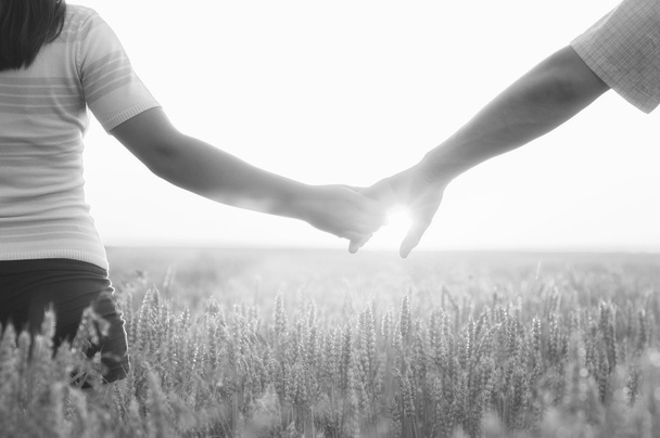 junges Paar Händchen haltend im Weizenfeld an einem sonnigen Sommertag - Foto, Bild