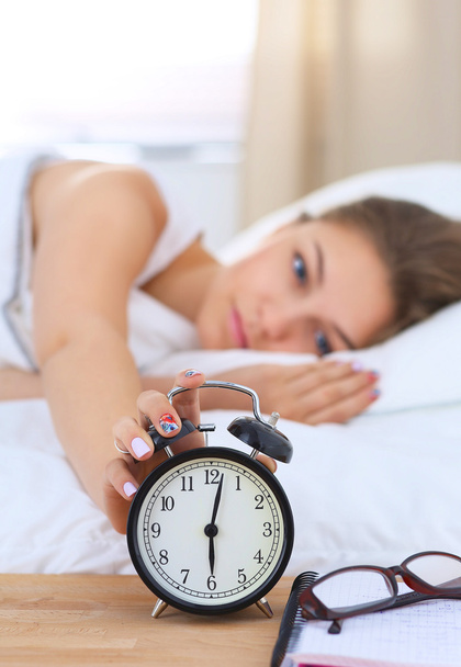Una mujer joven apagando su despertador por la mañana - Foto, Imagen