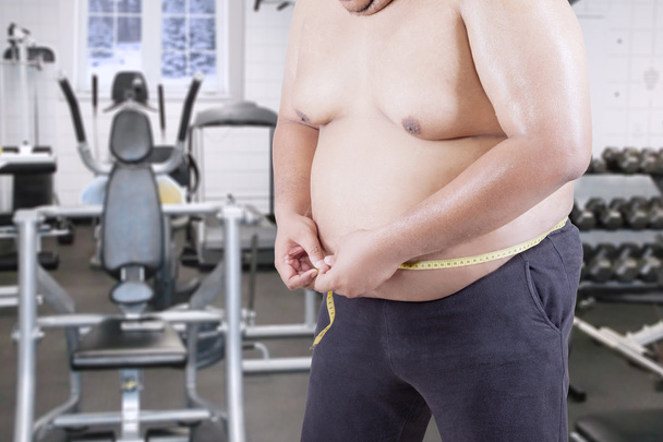 Overweight man measuring his belly at gym - Foto, Bild
