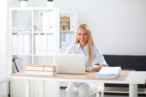 Attractive businesswoman sitting on a desk with laptop in the office - Foto, Bild