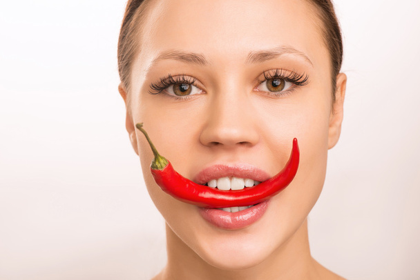 Young girl is holding red pepper with her teeth. - Fotoğraf, Görsel
