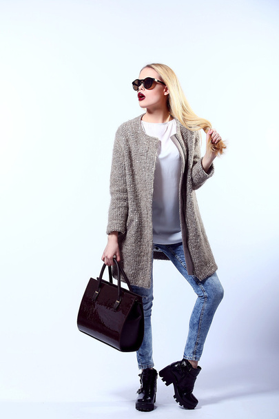 Sexy Beauty Girl. Fashion Blonde. Portrait of a girl dressed in grey coat, wearing a black bag, posing on a studio background. - Foto, Imagem