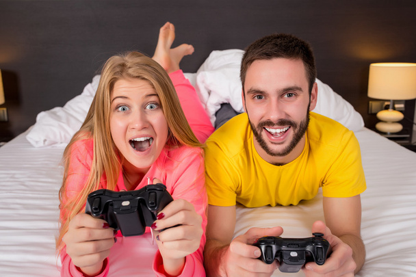 Счастливая молодая пара веселится, играя в видеоигры в постели
 - Фото, изображение