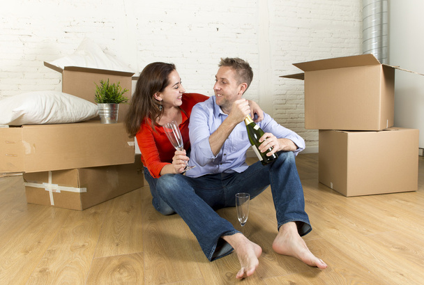 feliz casal sentado no chão desempacotando juntos comemorando com torrada de champanhe em movimento na nova casa
 - Foto, Imagem