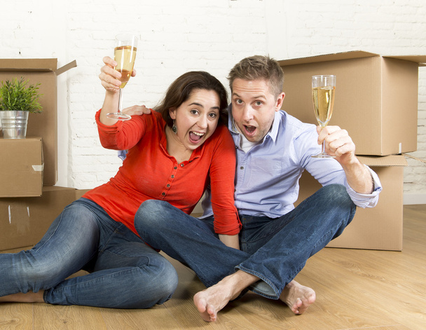 happy American couple sitting on floor unpacking together celebrating with champagne toast moving in a new house - Foto, afbeelding