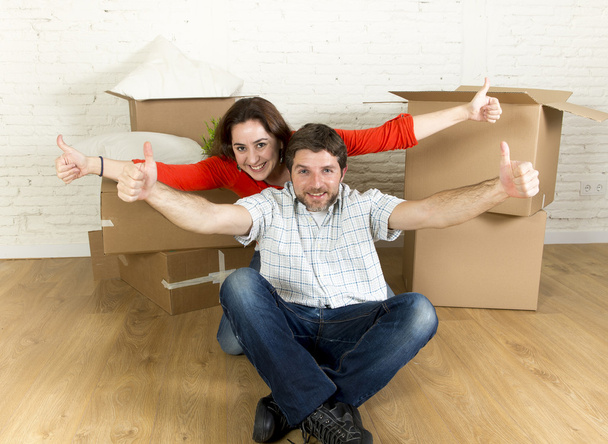 νεαρό ζευγάρι χαρούμενος που κάθεται στο πάτωμα μαζί γιορτάζει κινείται σε νέα Μονοκατοικία ή διαμέρισμα - Φωτογραφία, εικόνα