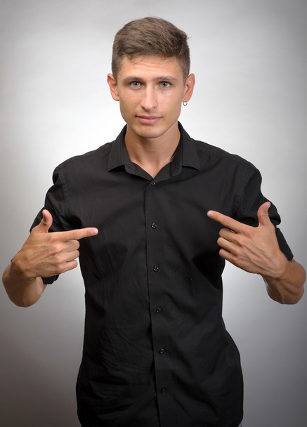 young smiling man in black pointing himself on a gray background - Foto, Bild