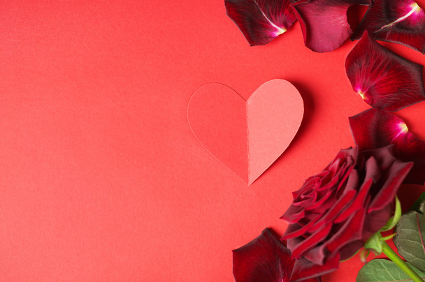 Dark red rose, petals and a paper heart on a red background - Photo, Image