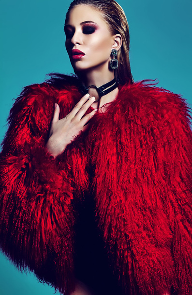 fashion glamor stylish swag young woman model in hipster red fur coat with bright makeup on blue background - Foto, afbeelding