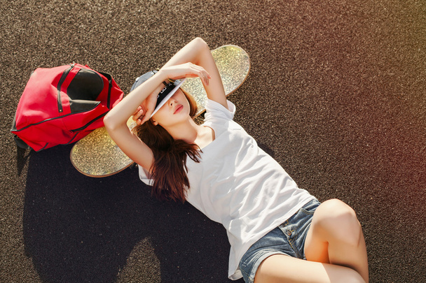 woman  lying on the ground with skateboard and backpack - Fotó, kép
