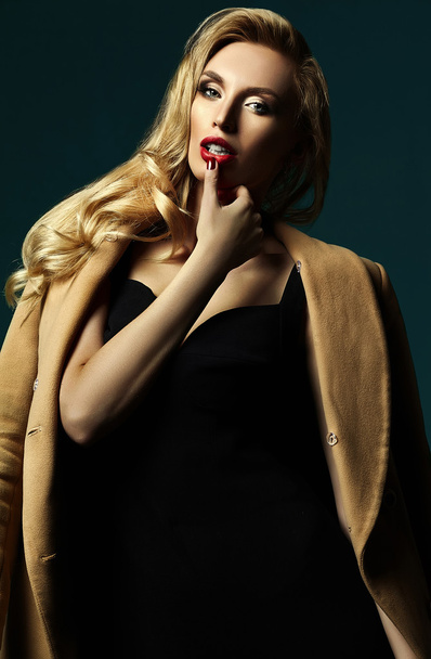 sensual glamour portrait of beautiful blond woman model lady with fresh makeup in classic black costume and overcoat touching lips - Zdjęcie, obraz