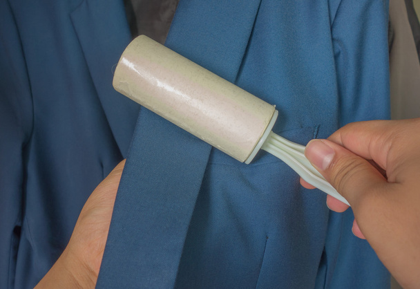 Dry cleaning and business theme: a man hand with blue suit holding a white sticky brush for cleaning clothes and furniture from dust - Photo, Image