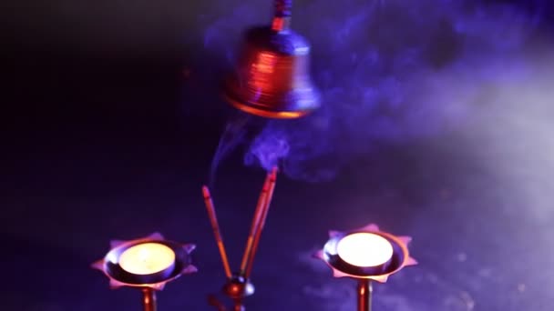 Ręczny dzwonek na ciemnym niebieskim tle z czerwonym filtrem światła i kadzidła - Materiał filmowy, wideo
