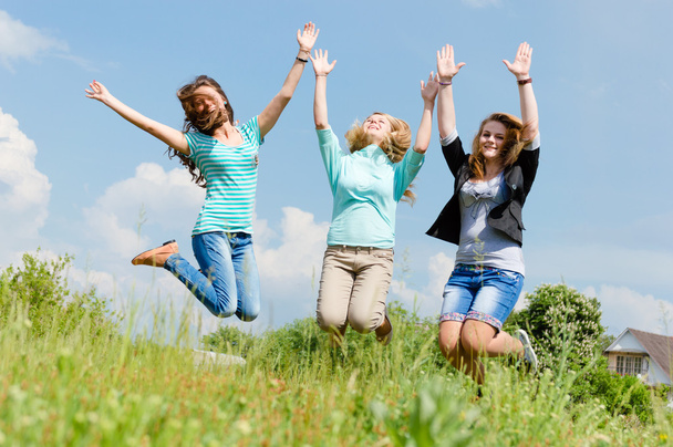 Tres chicas cogidas de la mano saltando en el campo de verano
 - Foto, imagen