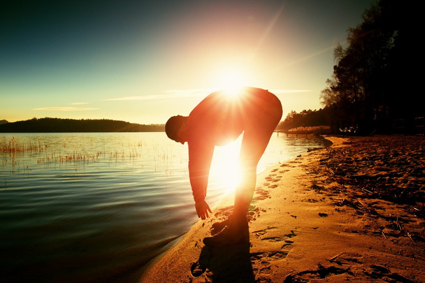 Silueta sportovní aktivní dospělé muže, běh a cvičení na pláži. Klidná voda, ostrov a pozadí nebe. - Fotografie, Obrázek