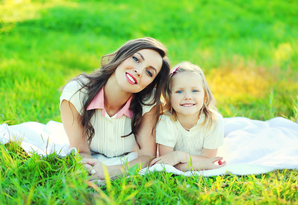 Happy mother and child daughter lying together on grass in summe - Photo, image