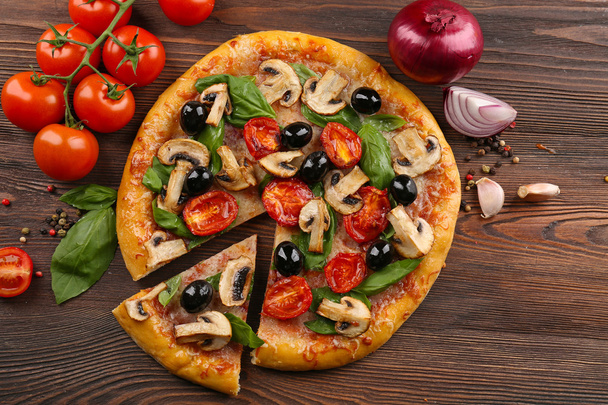 Sliced delicious tasty pizza with vegetables on wooden table - Zdjęcie, obraz