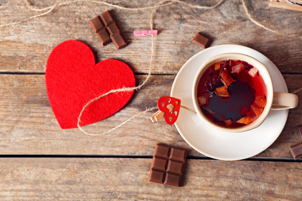 Cup of tea with red heart and piece of chocolate on wooden background closeup - Φωτογραφία, εικόνα