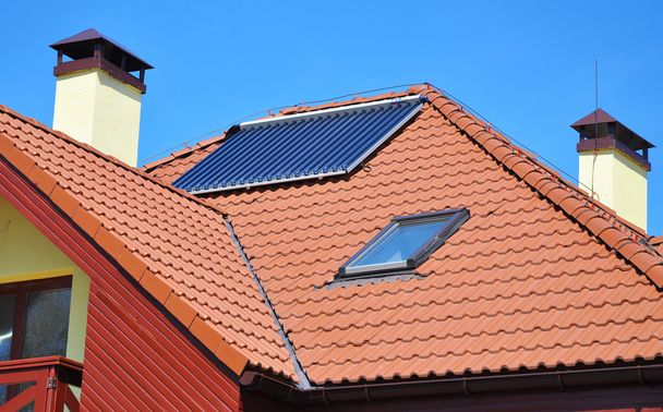 Conceito de eficiência energética. Closeup do aquecimento solar do painel de água no telhado da casa telha vermelha com proteção contra raios, clarabóias, chaminé e janela do telhado
 - Foto, Imagem