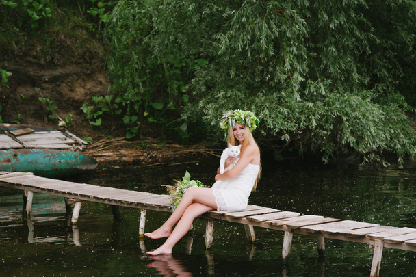 Beautiful girl wearing a crown sitting on a wooden bridge with a cat - Fotografie, Obrázek