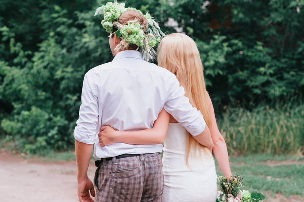 Happy young couple with a bouquet and a wreath embracing and kissing - Foto, Imagen