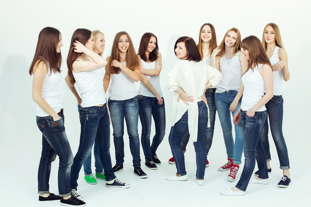 Onnellinen yhdessä käsite. Ryhmäkuva terveistä tytöistä valkoisissa t-paidoissa ja sinisissä farkuissa istumassa ja poseeraamassa valkoisella taustalla. Kopioi tilaa. Urbaani tyyli. Studiokuva
 - Valokuva, kuva