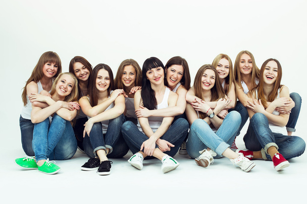 Feliz conceito em conjunto. Retrato de grupo de meninas saudáveis em camisetas brancas e jeans azuis sentados e posando sobre fundo branco. Espaço de cópia. Estilo urbano. Estúdio
 - Foto, Imagem