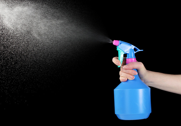 Hand holding spray bottle and spraying on black background - Foto, afbeelding