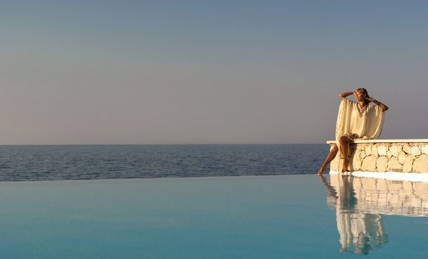 Mujer de estilo griego sentada en el borde de la piscina infinita
 - Foto, imagen