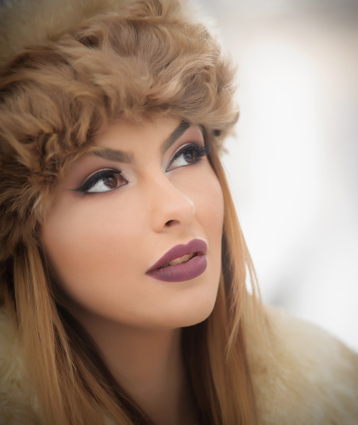 Attractive young Caucasian adult with brown fur cap. Beautiful blonde girl with gorgeous lips and eyes wearing fur hat, outdoor shot. Makeup - sensual long fair hair female art portrait, winter season - Foto, imagen