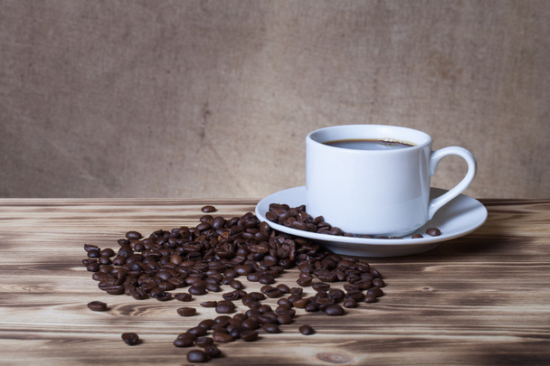 Coffee beans and coffee in white cup on wooden table opposite a  - Photo, Image