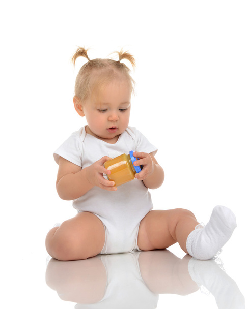 Infant Baby girl kid sitting and holdingin hands jar of child ma - Foto, Imagen