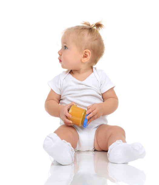 Baby girl sitting and holding jar of child mash puree food - Foto, afbeelding