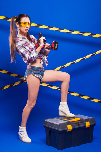 sexy brunette meisje bouwvakker met schroevendraaier op een blu - Foto, afbeelding