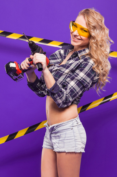 Sexy blonde construction worker with screwdriver on a purple bac - Foto, Bild