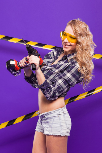Sexy blonde construction worker with screwdriver on a purple bac - Φωτογραφία, εικόνα